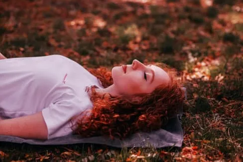 Woman with long red hair lying in leaves